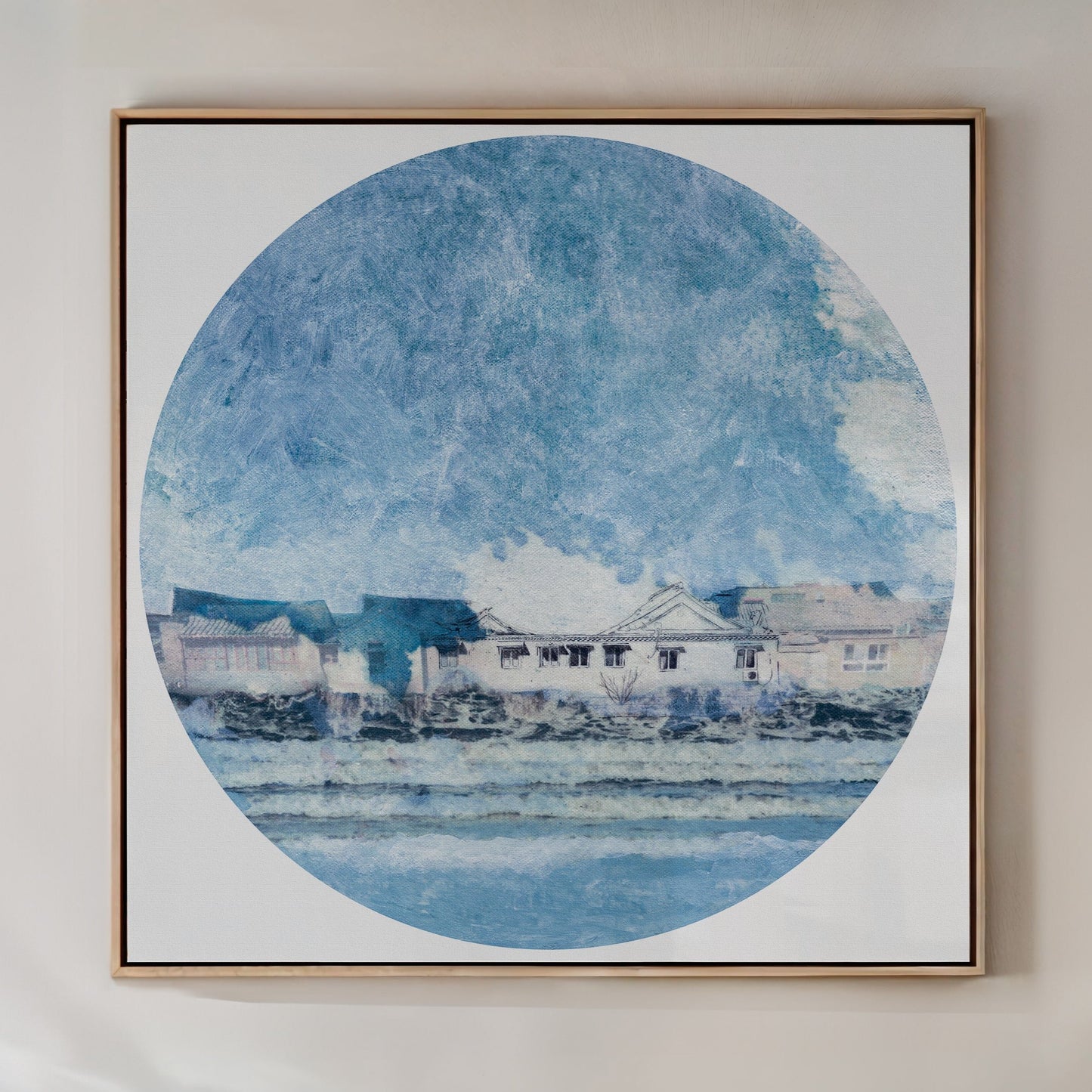 A framed art print featuring a circular water scene with houses along the shore and a clear blue sky.