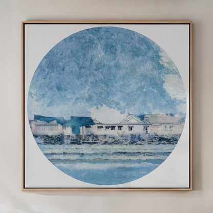 A framed art print featuring a circular water scene with houses along the shore and a clear blue sky.